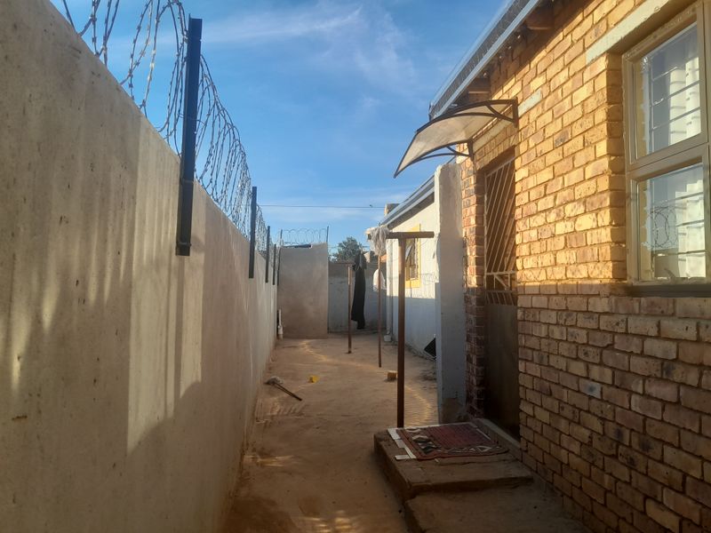 A narrow side passage featuring face brick exterior walls, a concrete boundary wall with razor wire security, and a small entrance awning.