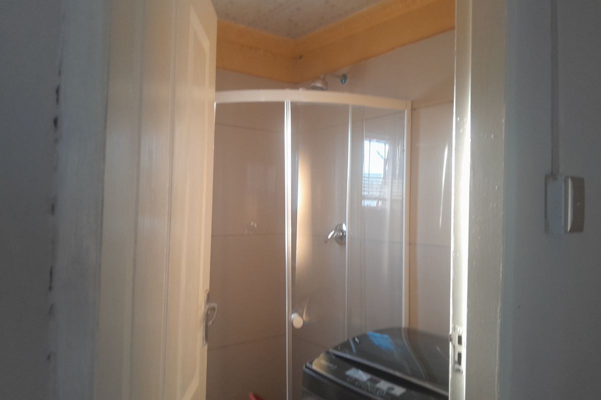 A compact bathroom featuring a corner shower enclosure with tiled walls and a ceiling cornice, showing signs of wear on the door frame.