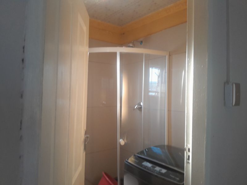 A compact bathroom featuring a corner shower enclosure with tiled walls and a ceiling cornice, showing signs of wear on the door frame.