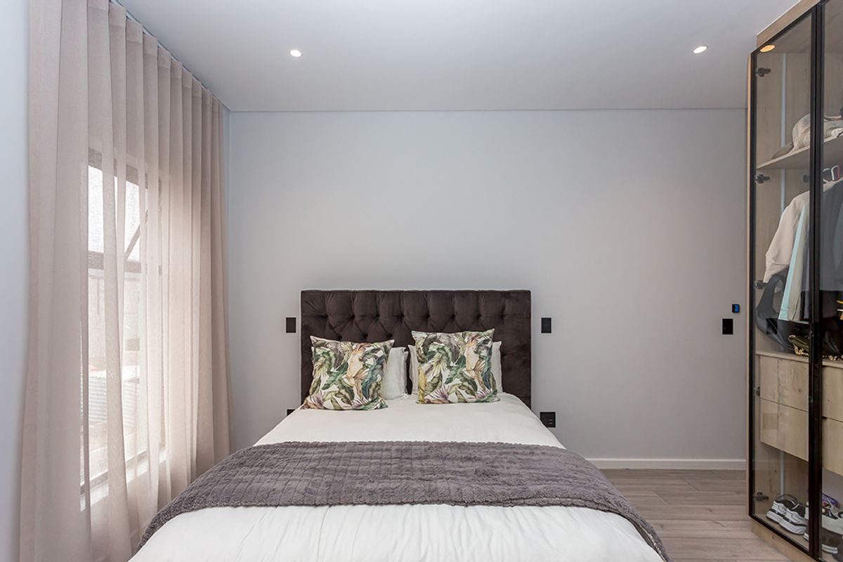 A modern, well-maintained bedroom featuring recessed downlights, light-toned laminate flooring, and a sleek built-in wardrobe with glass doors.