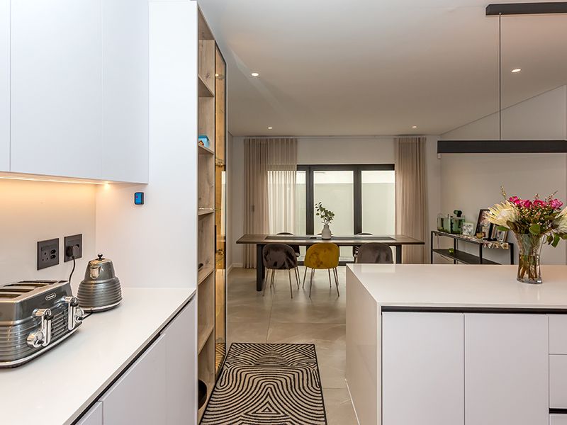 Modern open-plan kitchen and dining area featuring sleek white cabinetry, a central island, stone countertops, and large sliding doors leading to the exterior.