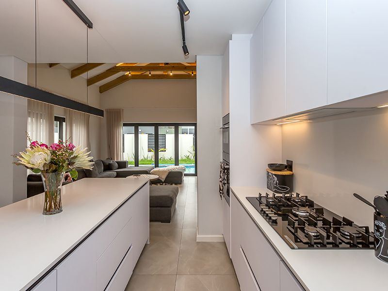 Modern open-plan kitchen featuring sleek handleless cabinetry, stone countertops, and a gas hob, flowing seamlessly into a spacious living area with exposed timber beams.