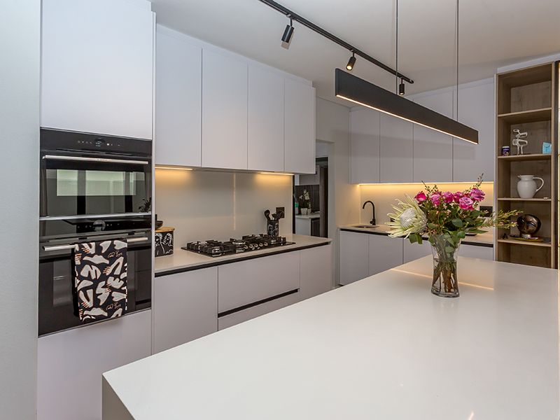 Modern kitchen featuring a large island with quartz countertops, built-in oven and microwave, gas hob, and sleek integrated cabinetry with ambient lighting.