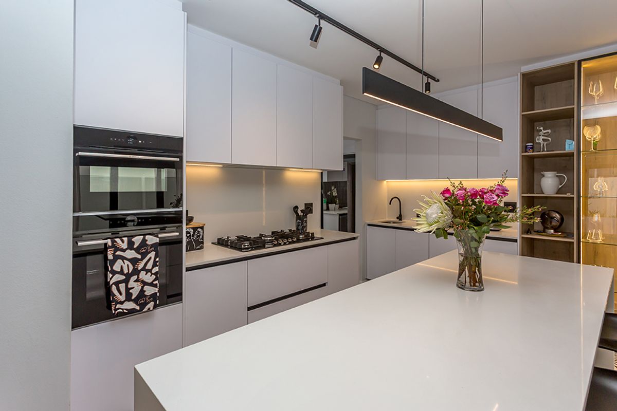 Modern kitchen featuring a large island with quartz countertops, built-in oven and microwave, gas hob, and sleek integrated cabinetry with ambient lighting.