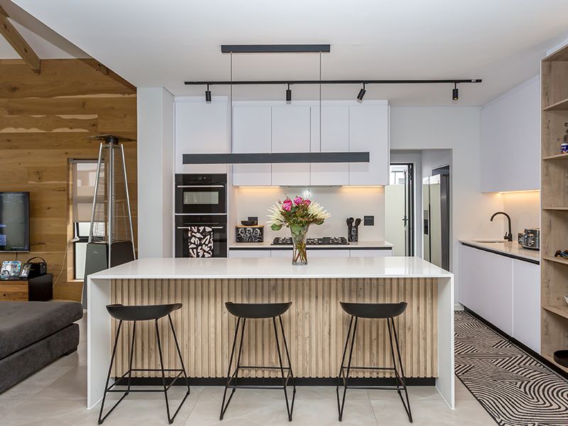 Modern open-plan kitchen featuring a central island with stone countertops, integrated appliances, timber wall accents, and stylish track lighting.