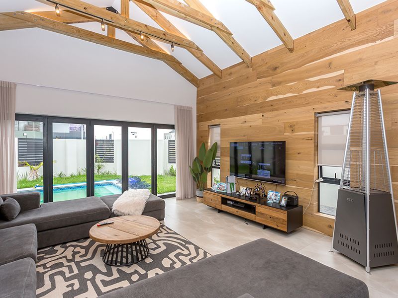 Spacious living room featuring high vaulted ceilings with exposed timber trusses, natural wood wall paneling, and large bi-fold doors opening to the pool area.