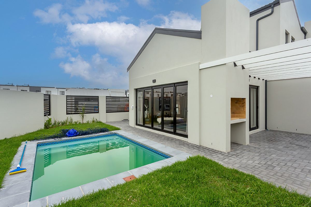 Rear exterior view featuring a swimming pool, paved patio area with a built-in braai, and a pergola, perfect for outdoor entertaining.