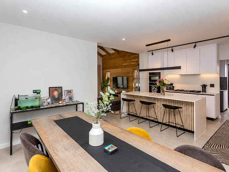 Modern open-plan living and kitchen area featuring a sleek kitchen island, contemporary cabinetry, integrated appliances, and warm timber wall accents.