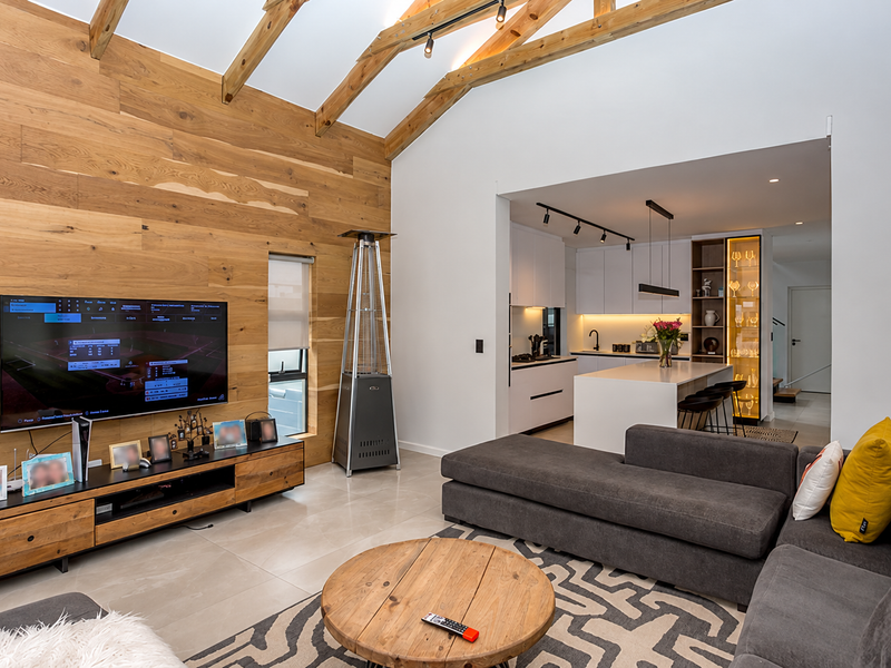 Modern open-plan living area featuring high vaulted ceilings with exposed timber trusses, wood-paneled feature wall, and a sleek, contemporary kitchen with island.