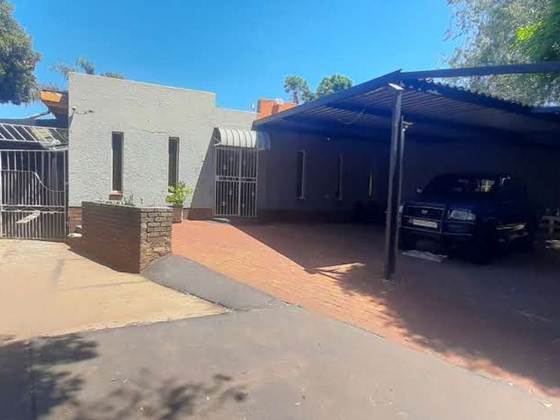 Front exterior view featuring a paved driveway, a covered carport, and secure gated access with brick boundary walls.