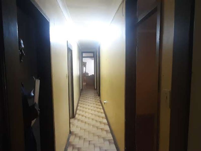 A long, narrow hallway featuring parquet flooring and multiple access points to adjacent rooms, currently showing signs of wear and dated finishes.