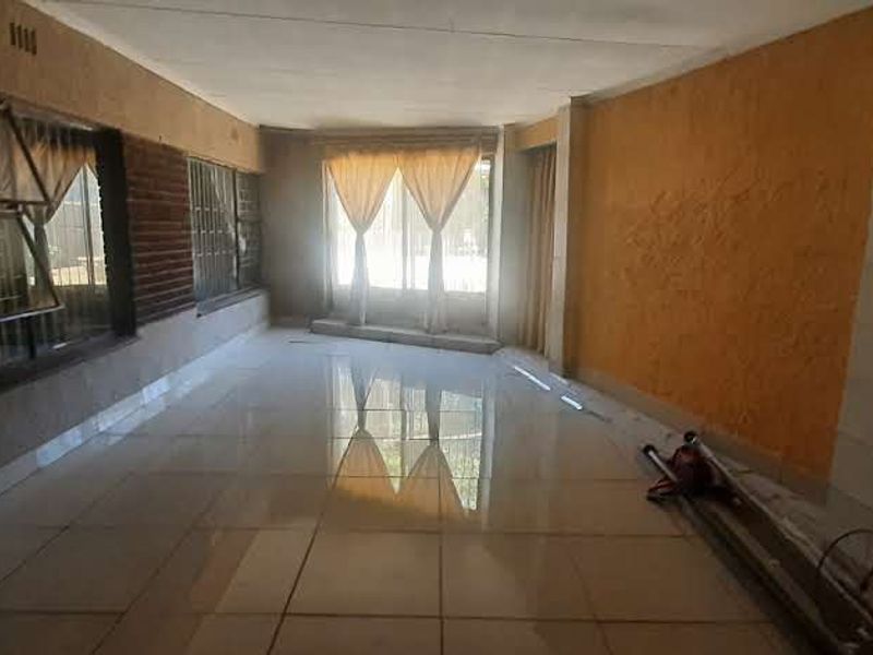 An empty, spacious living area featuring tiled flooring and large windows, offering a blank canvas for renovation and interior design updates.