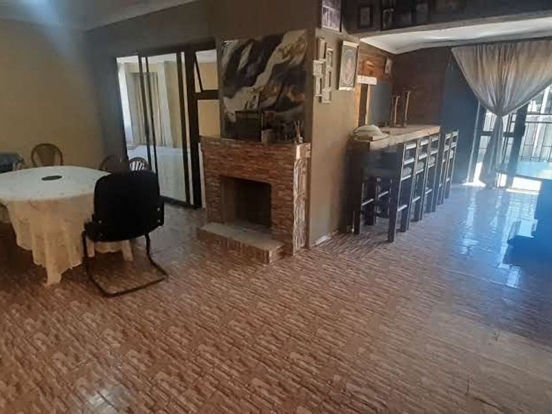 Spacious open-plan living and dining area featuring a stone-clad fireplace, tiled flooring, and a built-in bar counter with access to the exterior.
