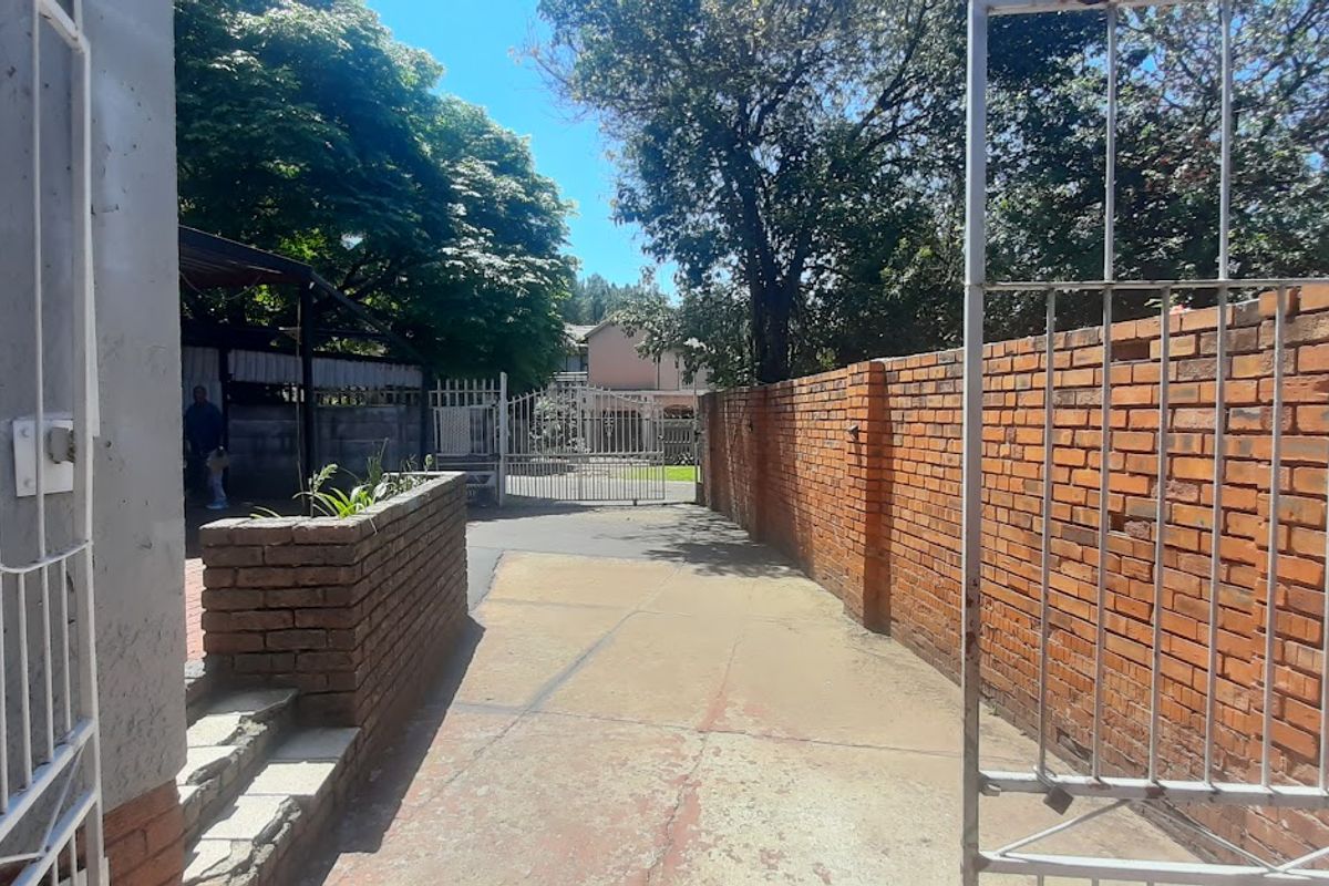 A view of the property entrance featuring a concrete driveway, brick boundary walls, and a metal security gate.