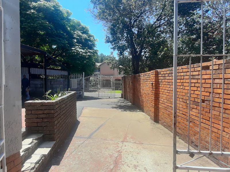 A view of the property entrance featuring a concrete driveway, brick boundary walls, and a metal security gate.