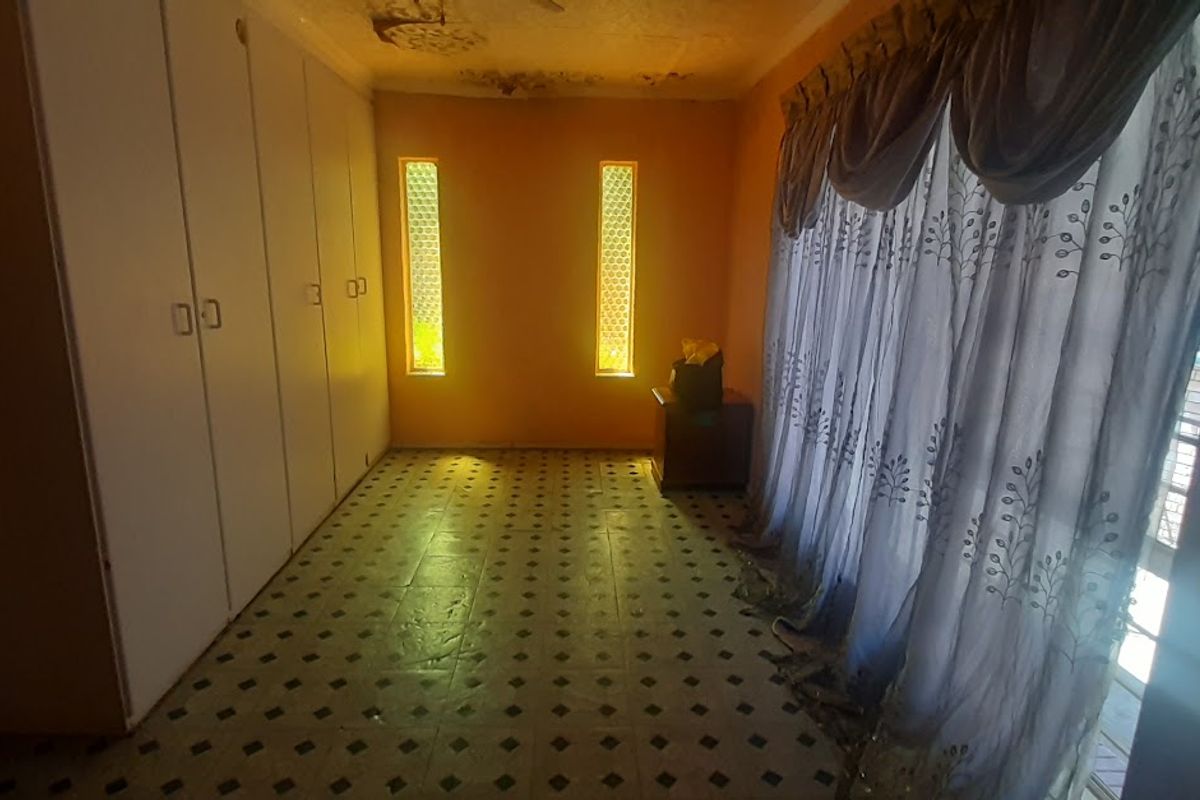 A bedroom featuring built-in cupboards, tiled flooring, and vertical accent windows, currently showing signs of ceiling water damage requiring repair.