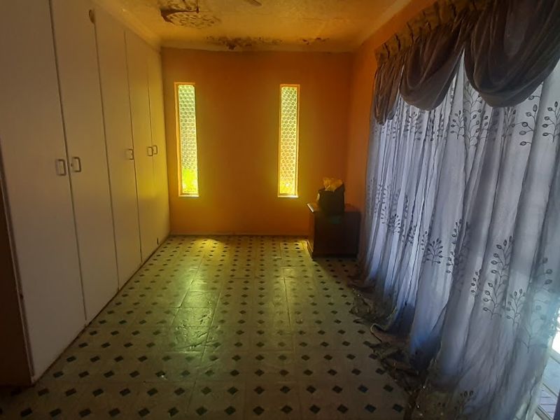 A bedroom featuring built-in cupboards, tiled flooring, and vertical accent windows, currently showing signs of ceiling water damage requiring repair.