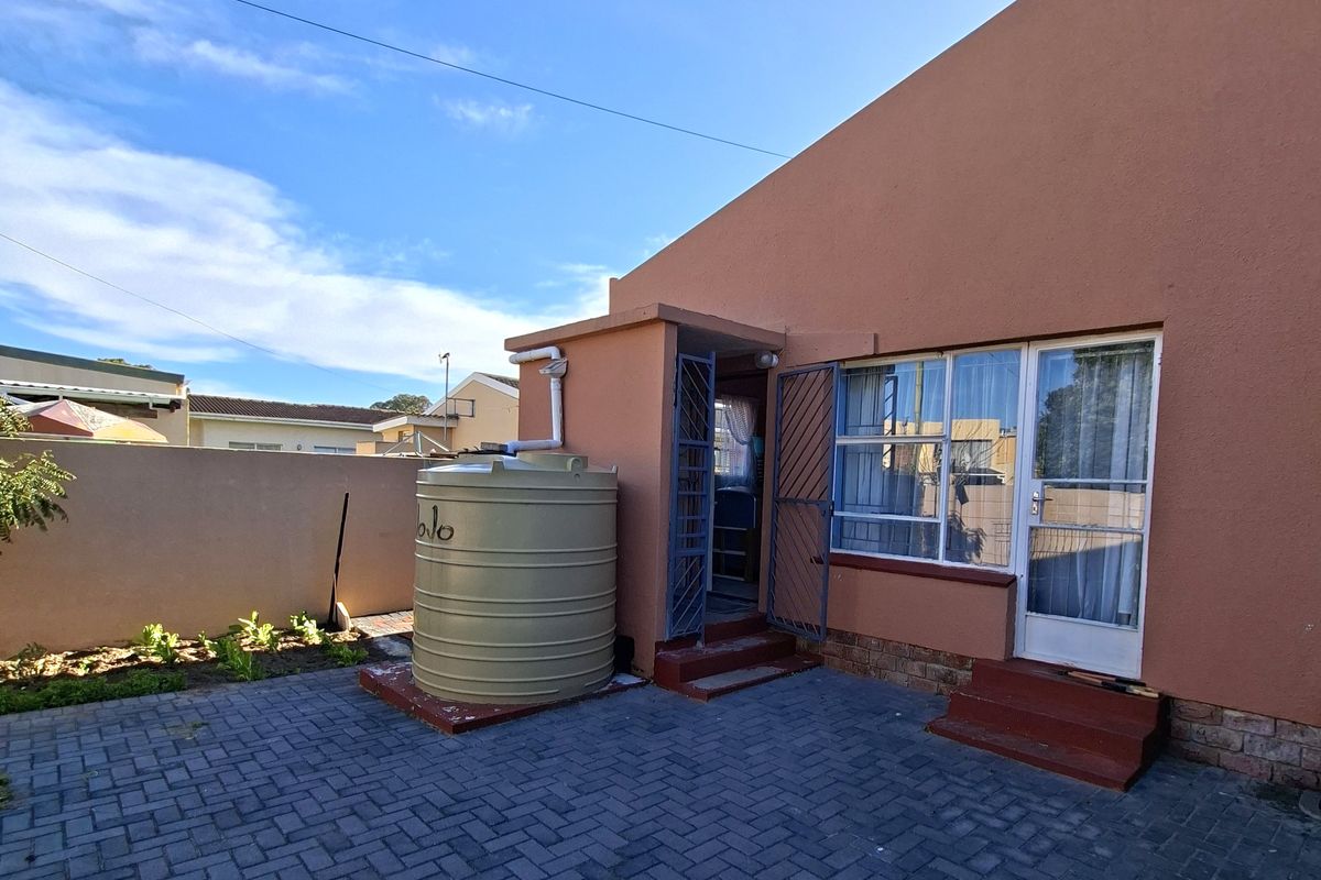 Rear exterior view featuring a paved courtyard, water storage tank, and secure access points to the main dwelling.