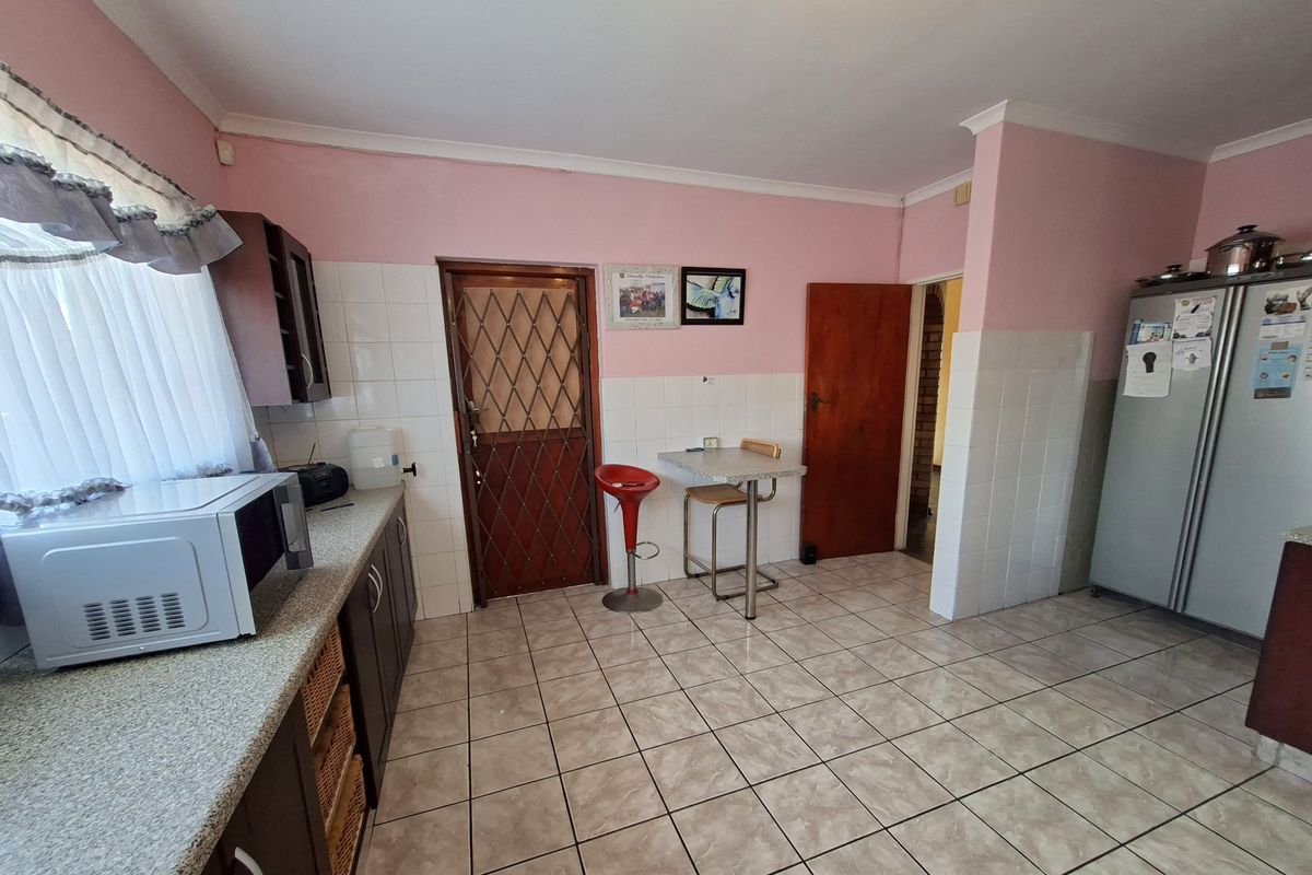 A functional kitchen featuring tiled flooring, tiled splashbacks, and built-in cabinetry with laminate countertops, providing a practical workspace with direct access to adjacent areas.