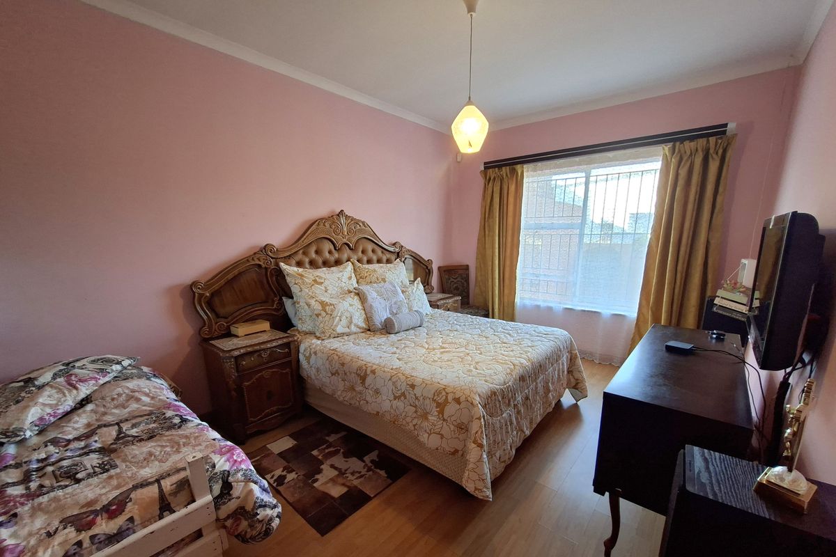 A bedroom featuring laminate flooring, a coved ceiling, and a window fitted with security bars.