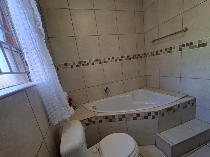 A functional bathroom featuring a built-in corner bathtub, tiled walls with decorative accents, and a standard toilet.
