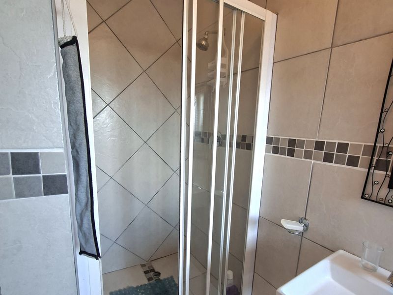 A functional bathroom featuring a tiled shower enclosure with a sliding door and a wall-mounted basin with neutral ceramic wall and floor tiling.