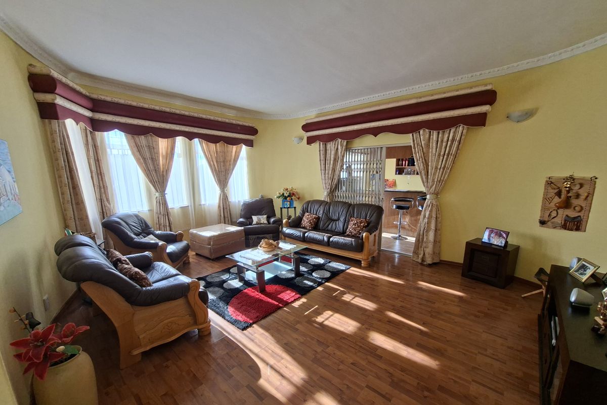 Spacious living room featuring laminate flooring, decorative ceiling cornices, and large windows with integrated pelmets, providing a comfortable and well-lit living space.