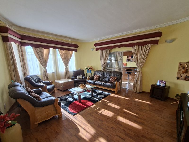 Spacious living room featuring laminate flooring, decorative ceiling cornices, and large windows with integrated pelmets, providing a comfortable and well-lit living space.