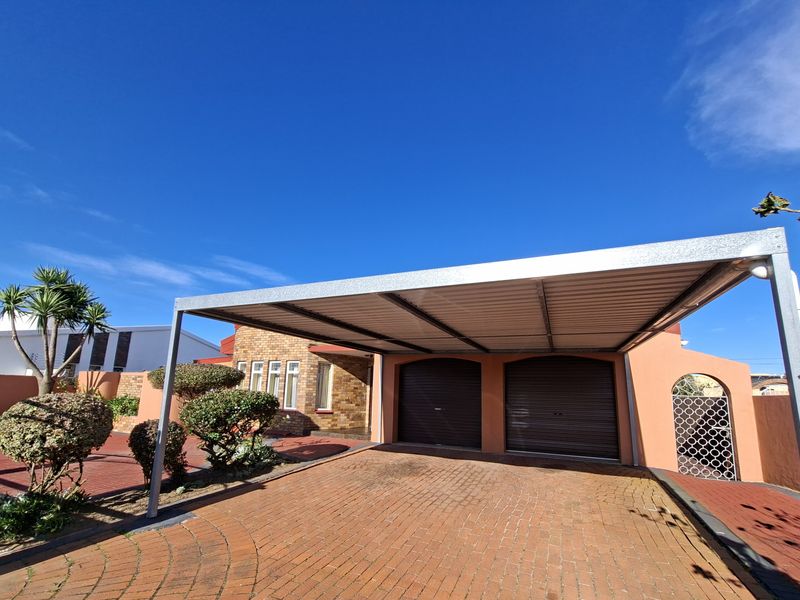 A well-maintained exterior view featuring a double carport, double garage doors, and a paved driveway leading to a facebrick residential facade.