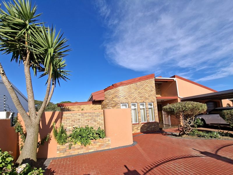 Front exterior view of the house featuring a brick facade, paved driveway, and a covered carport area with established garden elements.