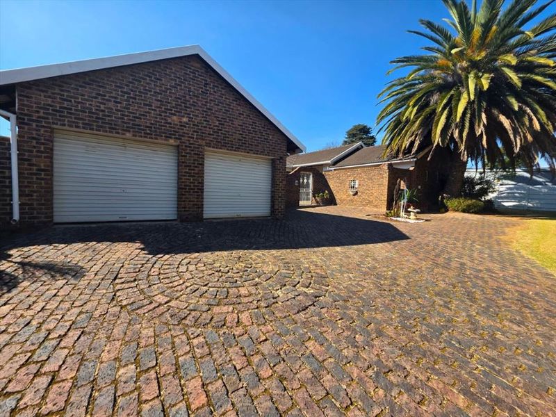 Front exterior view of the property featuring a double garage, brick facade, and a circular patterned brick driveway.