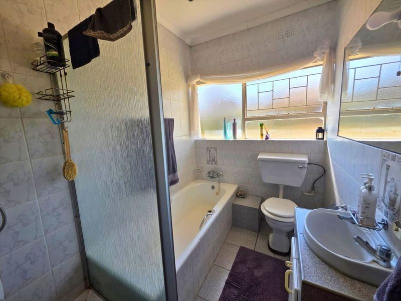 A functional bathroom featuring a bathtub, shower screen, toilet, and vanity basin with tiled walls and flooring.