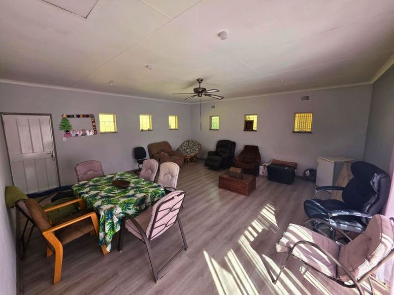 Spacious living area featuring laminate flooring, a ceiling fan, and multiple small windows providing natural light.
