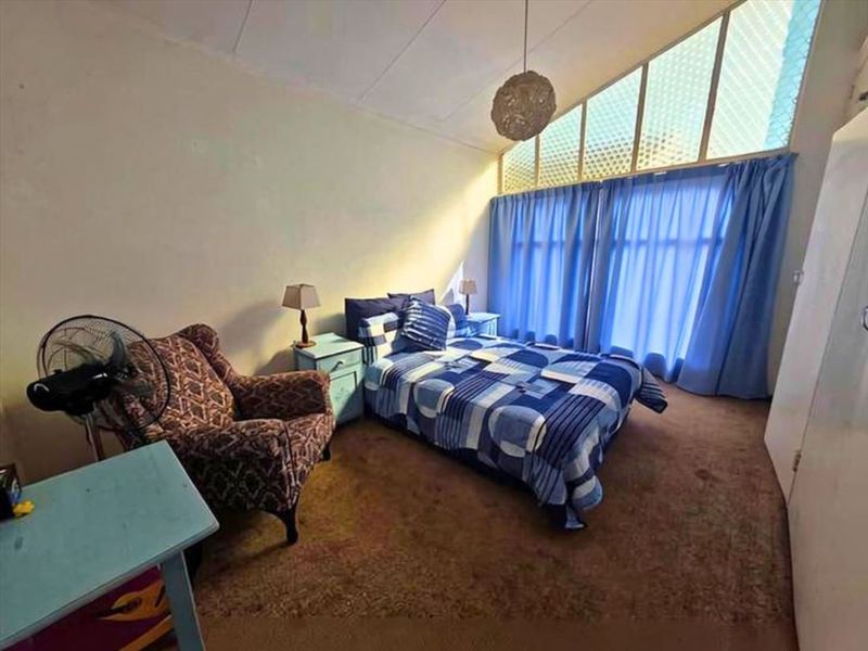 A bedroom featuring a raked ceiling, built-in wardrobe, and large windows allowing natural light. The space would benefit from modern flooring and updated wall finishes.