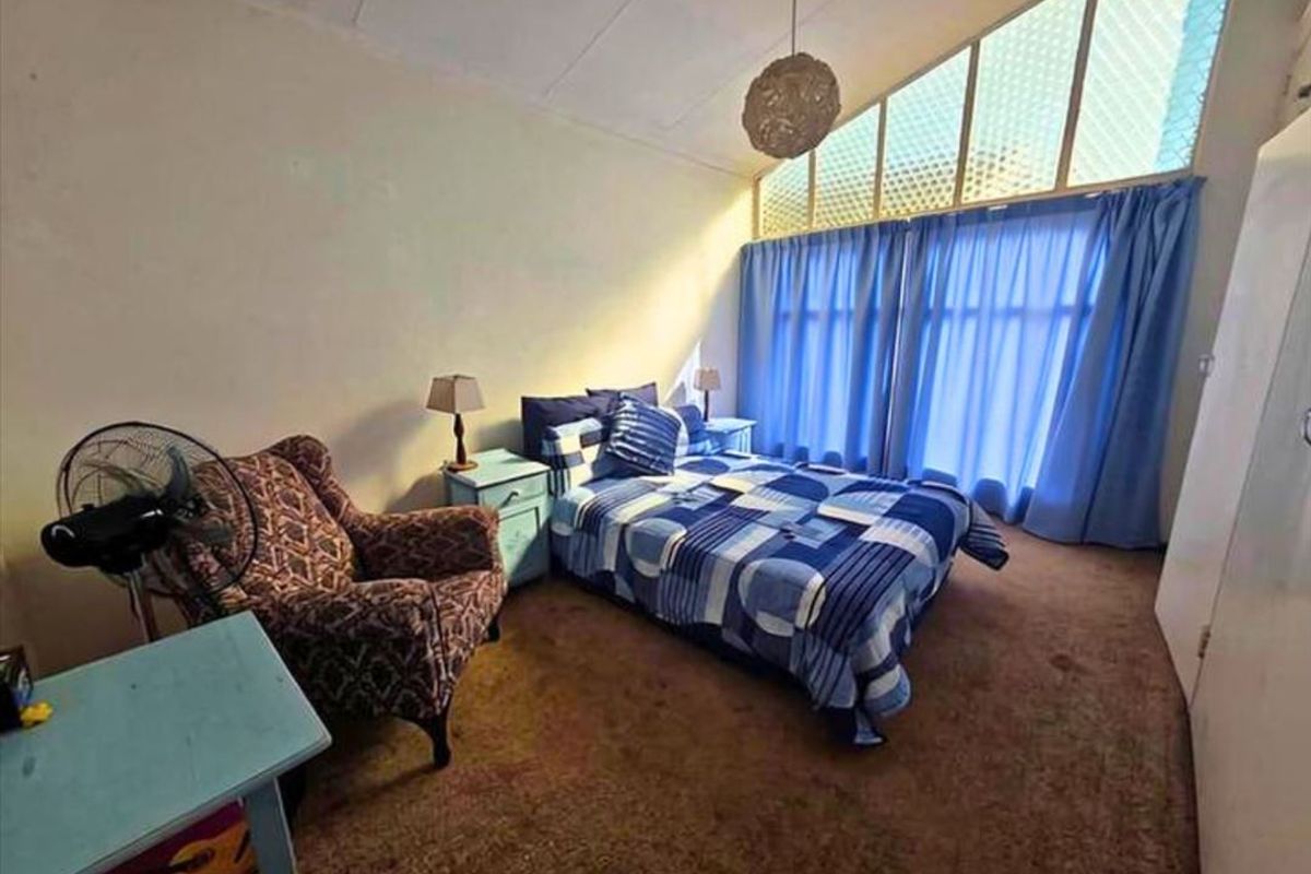 A bedroom featuring a raked ceiling, built-in wardrobe, and large windows allowing natural light. The space would benefit from modern flooring and updated wall finishes.