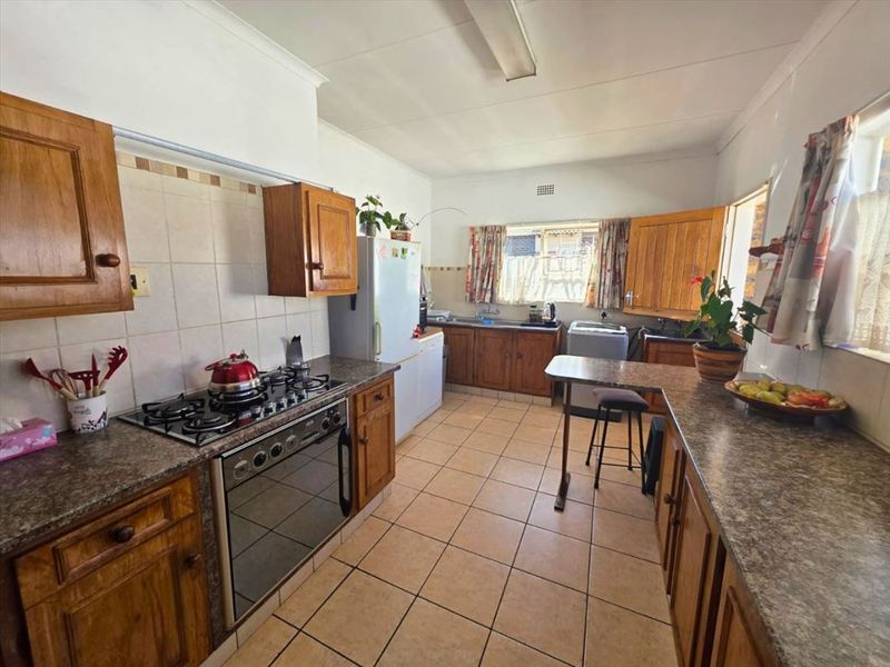 A functional kitchen featuring wooden cabinetry, laminate countertops, a gas hob, and tiled flooring, offering a classic layout with ample storage space.
