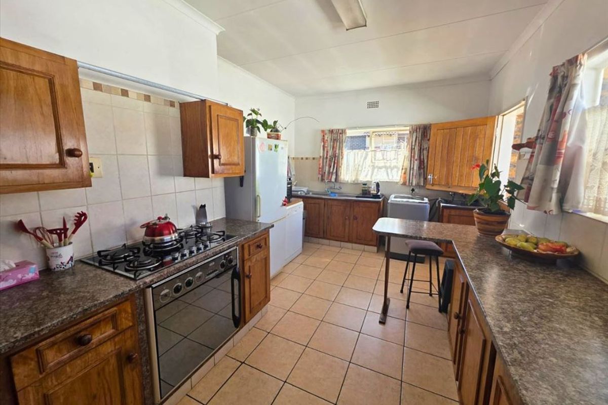 A functional kitchen featuring wooden cabinetry, laminate countertops, a gas hob, and tiled flooring, offering a classic layout with ample storage space.
