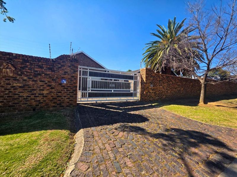 Front exterior view featuring a secure sliding driveway gate, brick boundary wall with electric fencing, and a paved cobblestone driveway.