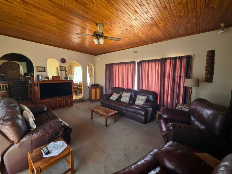 Spacious living room featuring a warm timber tongue and groove ceiling, ceiling fan, and classic arched doorways leading to adjacent living areas.