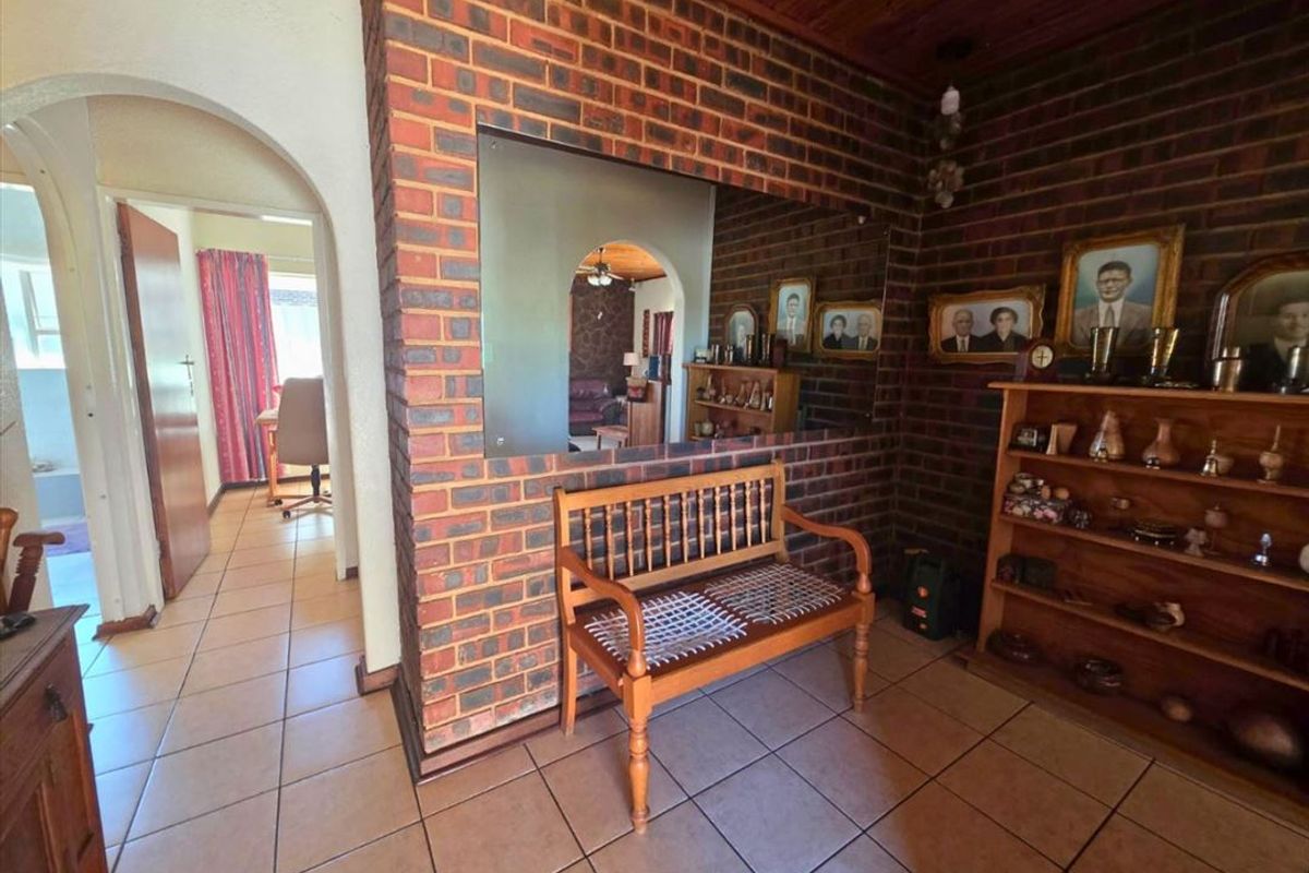 Living area featuring exposed brick walls, timber ceiling, and ceramic floor tiles, with an open archway leading to adjacent rooms.