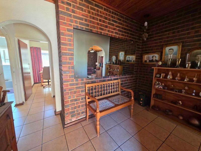 Living area featuring exposed brick walls, timber ceiling, and ceramic floor tiles, with an open archway leading to adjacent rooms.