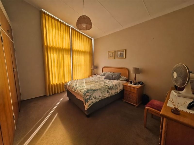 A well-lit bedroom featuring floor-to-ceiling windows and built-in wooden cupboards, offering a functional space with natural light.