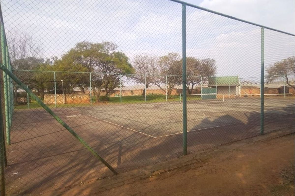 A fenced outdoor tennis court facility with a paved surface, showing signs of wear and age.