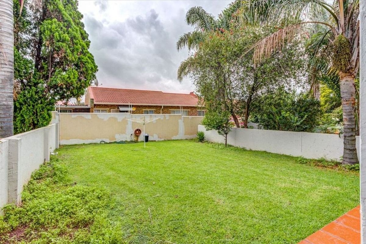 A private rear garden featuring a lawn area, mature trees, and a perimeter wall requiring maintenance.