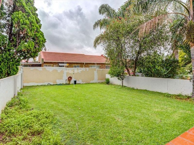 A private rear garden featuring a lawn area, mature trees, and a perimeter wall requiring maintenance.