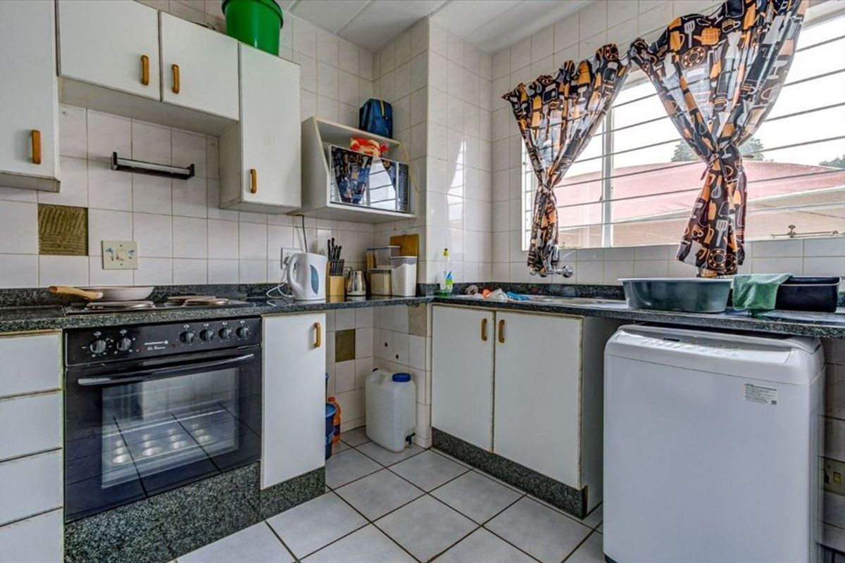 A functional kitchen featuring granite countertops, built-in oven, hob, and tiled finishes, offering a practical layout with ample storage cabinetry.