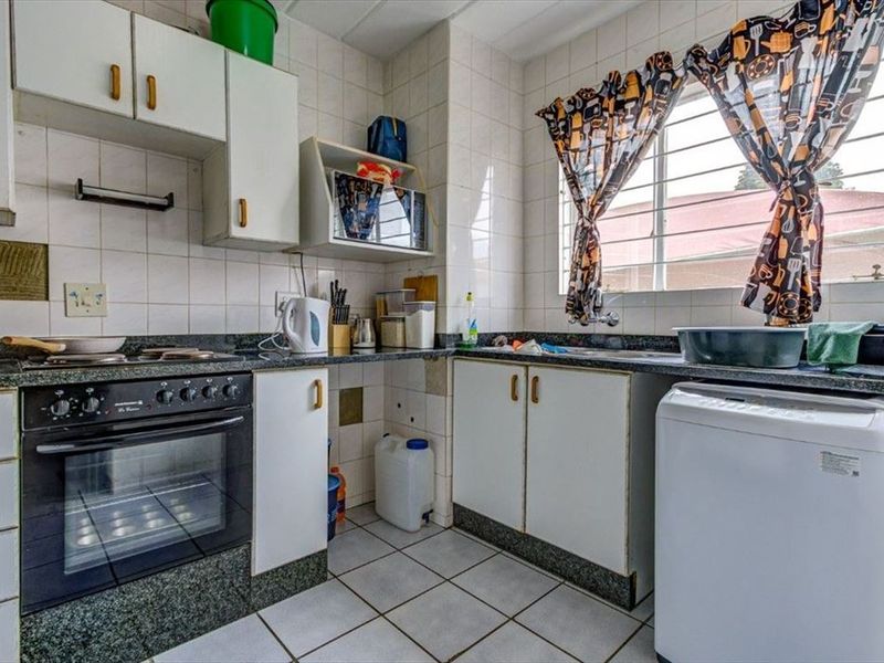 A functional kitchen featuring granite countertops, built-in oven, hob, and tiled finishes, offering a practical layout with ample storage cabinetry.