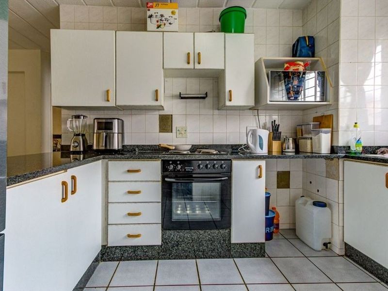 A dated kitchen featuring white cabinetry, granite countertops, and a built-in oven, offering a functional layout with potential for modern renovation.