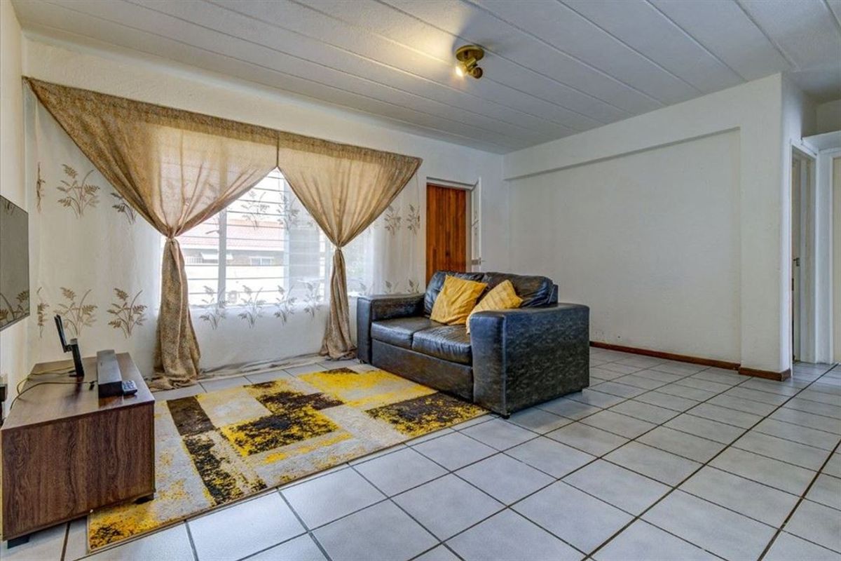A functional living room featuring tiled flooring, a window with security bars, and a wooden door, offering a neutral base for potential interior updates.