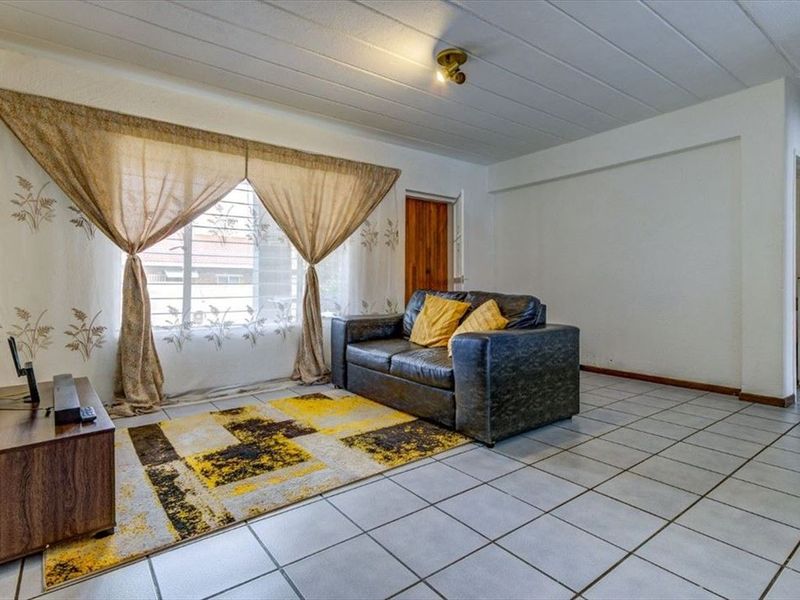 A functional living room featuring tiled flooring, a window with security bars, and a wooden door, offering a neutral base for potential interior updates.